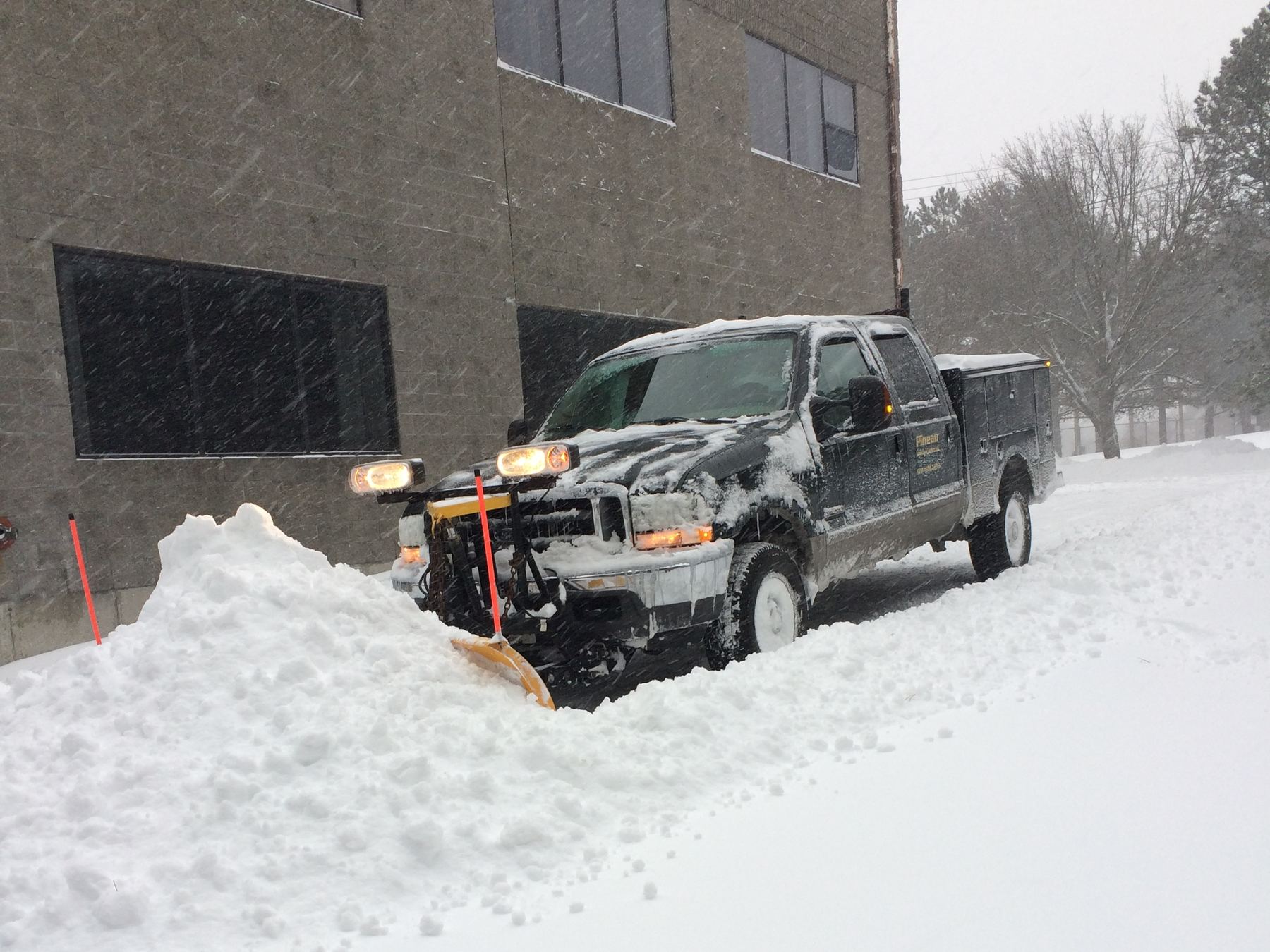 Pineau plow truck clearing snow beside a commercial office building